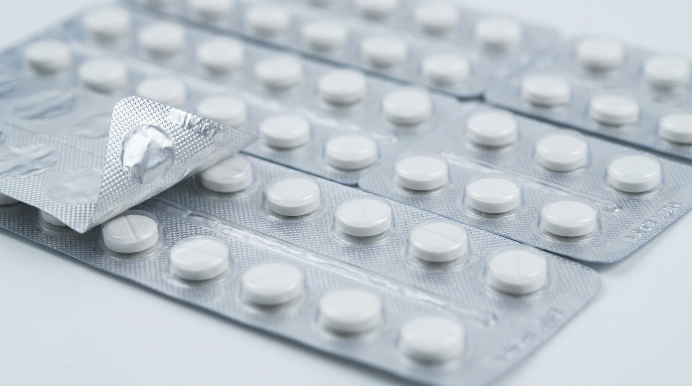 A close-up of transparent PVC blister packs containing small round white pharmaceutical tablets, arranged on a clean white surface with clear plastic blisters and aluminum foil backing visible